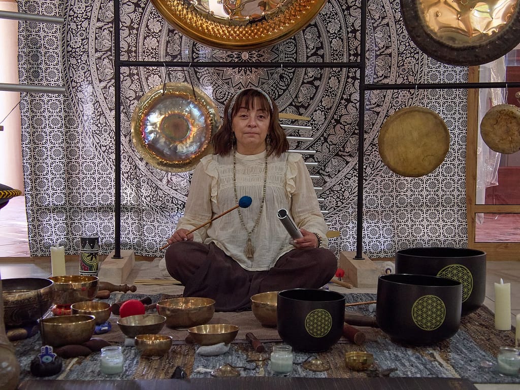 Aída Juárez, terapeuta de sonido de Eco Ancestral en Pachuca, sentada en postura de meditación rodeada de gongs sinfónicos, cuencos tibetanos de metal y cristal, y otros instrumentos terapéuticos.